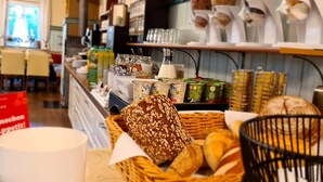 Mostrador de panadería con panes y pasteles variados, una máquina de café y un letrero en alemán.