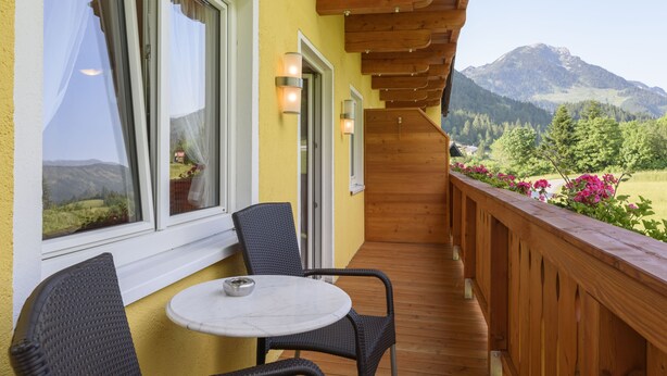 Balcón con barandilla de madera, una mesa y sillas, con vistas a un paisaje montañoso.