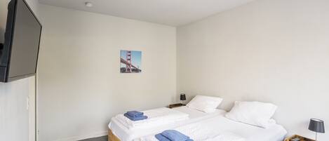 A hotel room with two beds, a flat-screen TV, a nightstand with a lamp, and a picture of the Golden Gate Bridge on the wall.