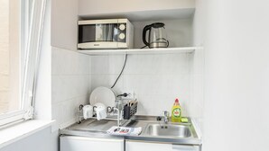 A compact kitchen with a microwave, kettle, and a small sink. - Icke Apartments (Berlin)
