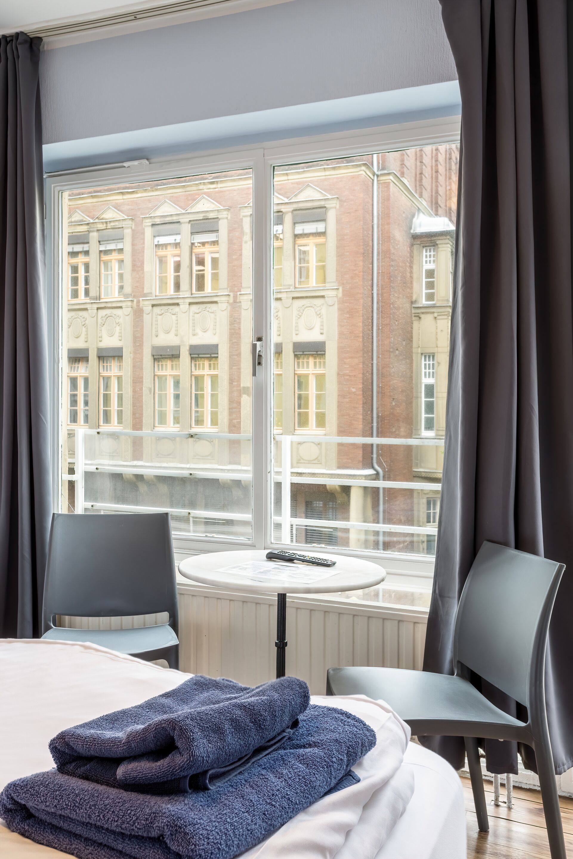 Habitación de hotel con cama, dos sillas, una mesita y vista a un edificio a través de una ventana.