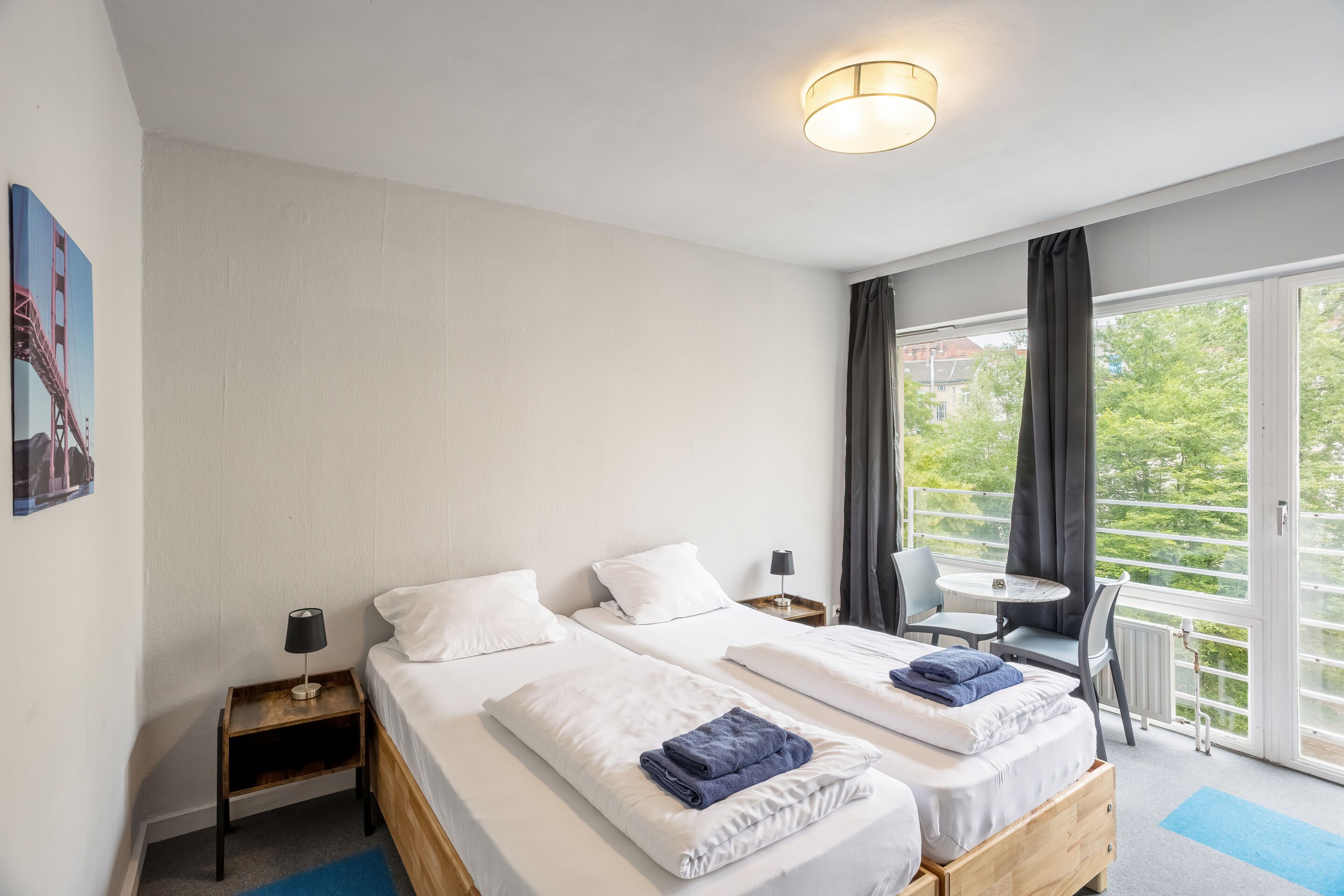 A hotel room with two beds, a small table, a chair, and a balcony with a view.