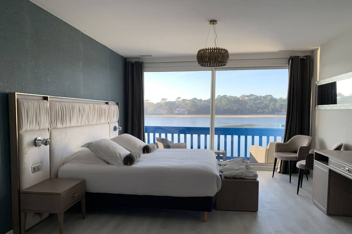 A modern hotel room with a large bed, a desk, a chair, and a view of a body of water.