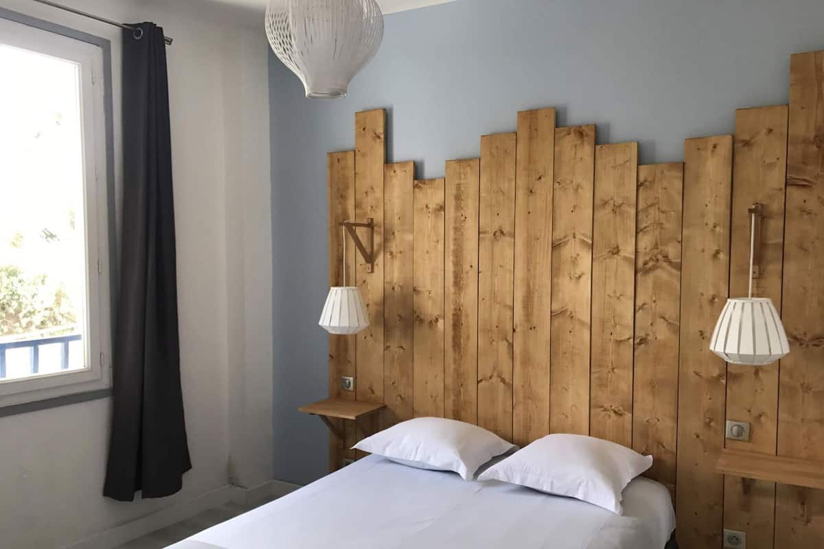 A bedroom with a wooden headboard, two bedside lamps, a bed with white linens, and a window with curtains.