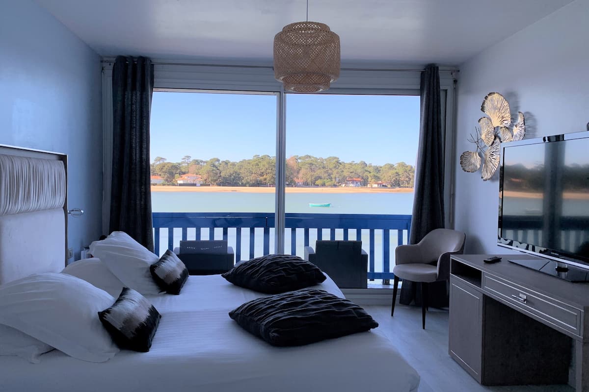 A hotel room with a bed, a TV, a desk, and a view of the sea.