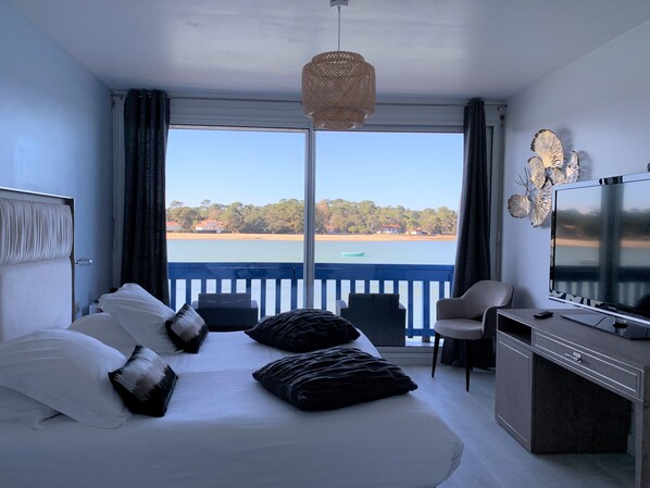 A hotel room with a bed, a TV, a desk, and a view of the sea.