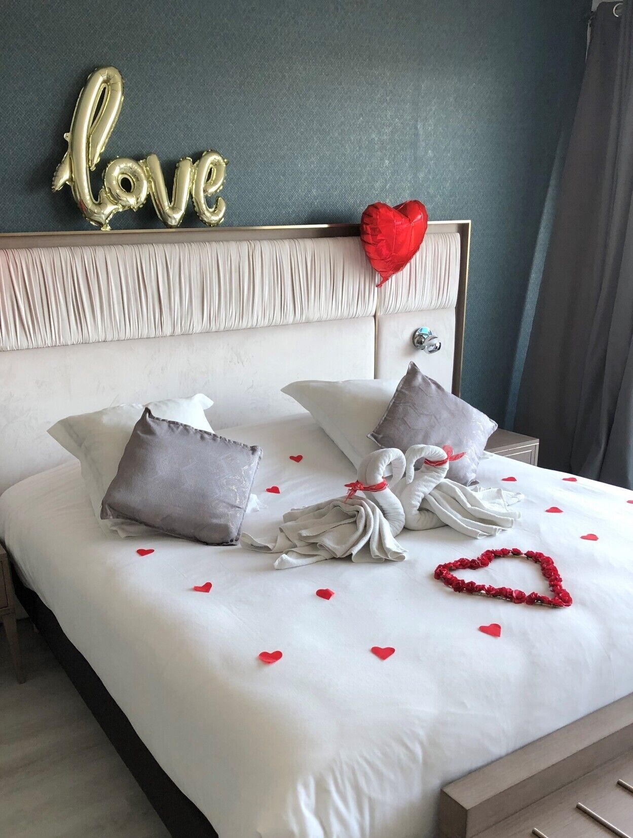 A neatly made bed with pillows, a heart-shaped decoration, and a 'love' sign on the headboard.