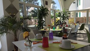 Un comedor con mesas, sillas y plantas en macetas.