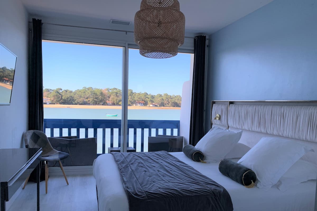 A hotel room with a bed, a desk, and a chair. There is a view of a body of water and trees outside the window.