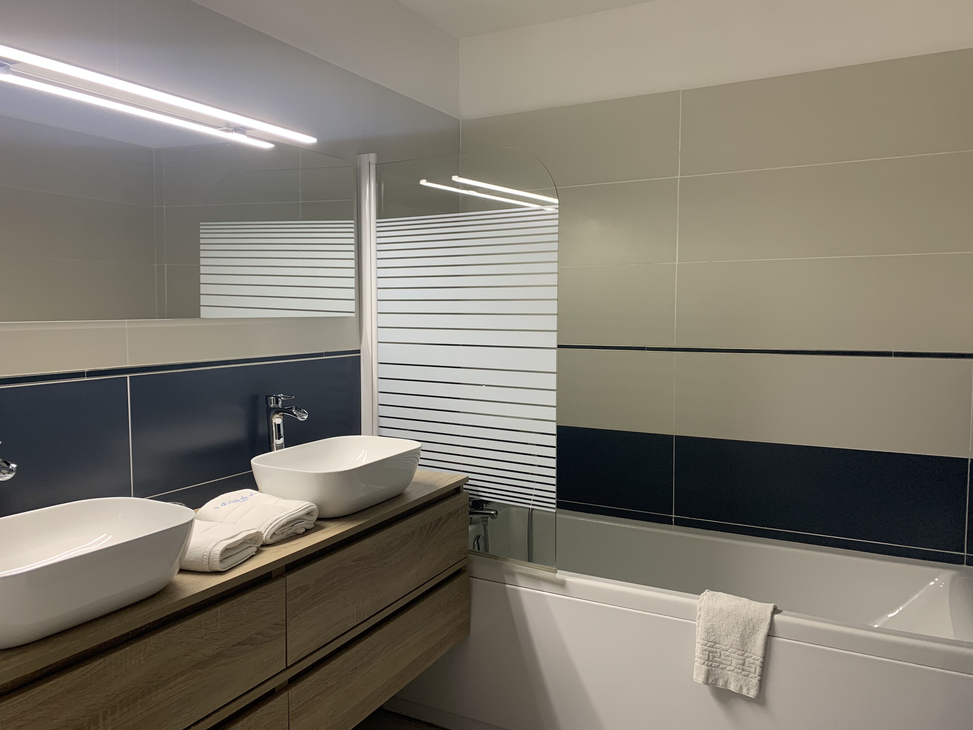A modern bathroom with a vanity, two sinks, a mirror, and a bathtub.