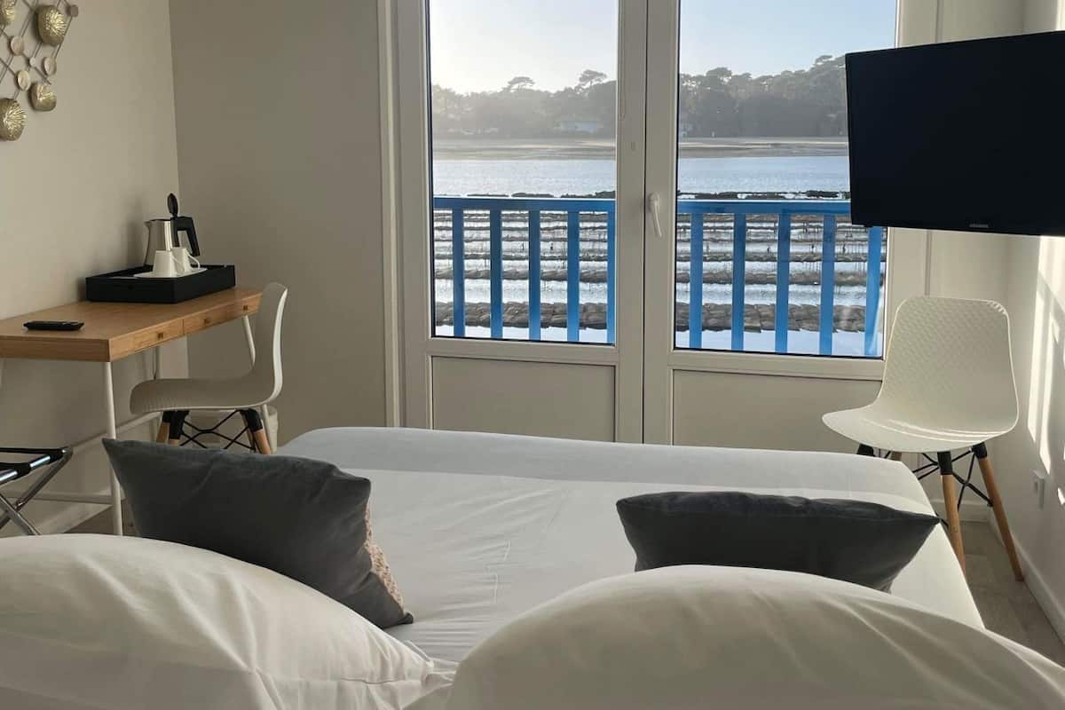 A hotel room with a bed, a desk, a chair, a TV, and a balcony with a view of the water.