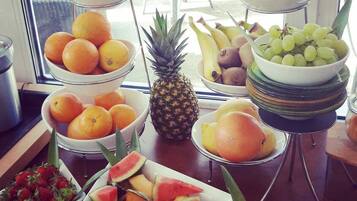 Une présentation de fruits et légumes comprenant divers fruits, comme des oranges, des raisins et des pastèques, disposés sur une table dans une pièce donnant sur un espace extérieur aménagé en salon.