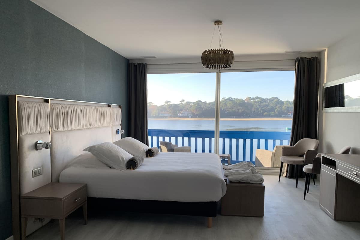 A modern hotel room with a large bed, a desk, and a view of a lake.