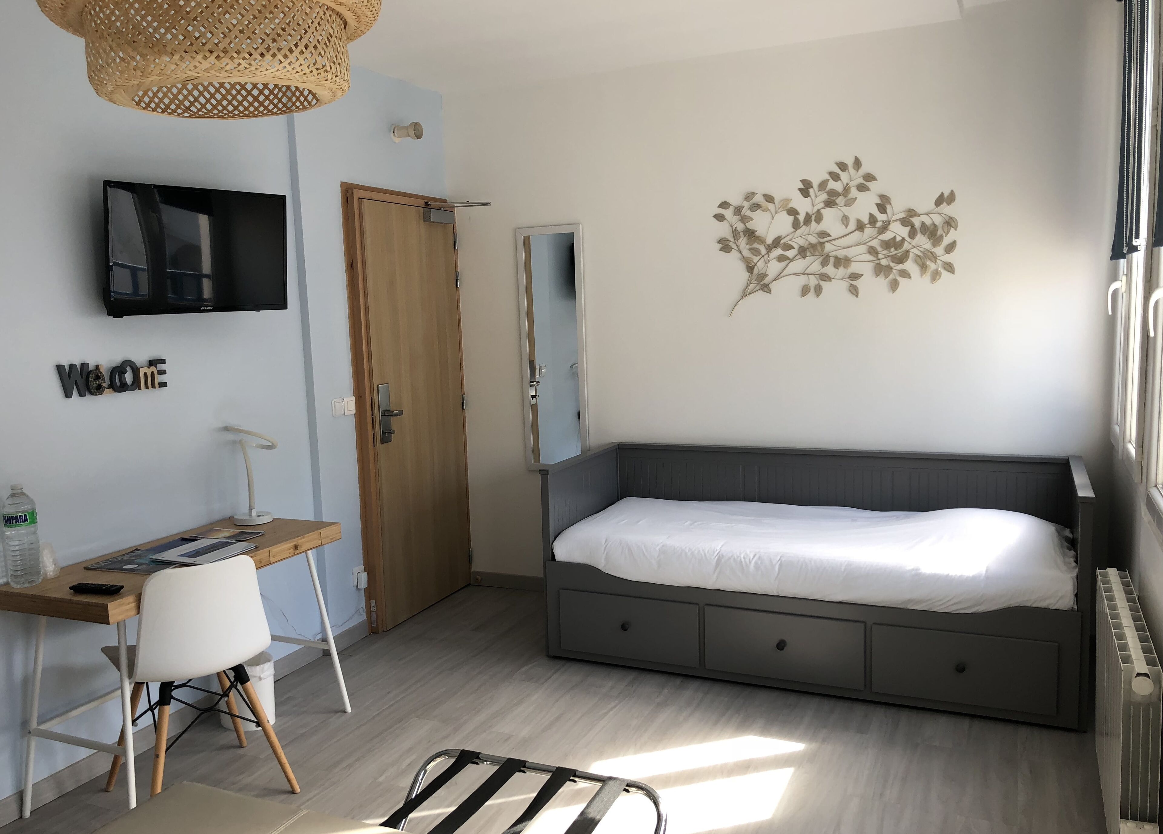 A bedroom with a bed, a desk, a chair, a TV, and a wall decoration.