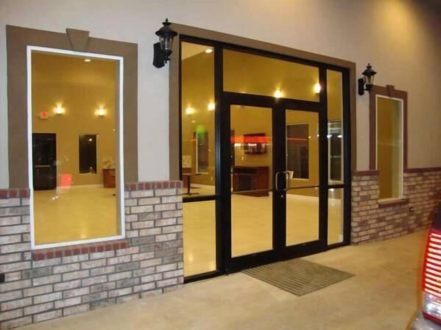 A hotel entrance with a glass door, brick walls, and a small outdoor area with a bench.