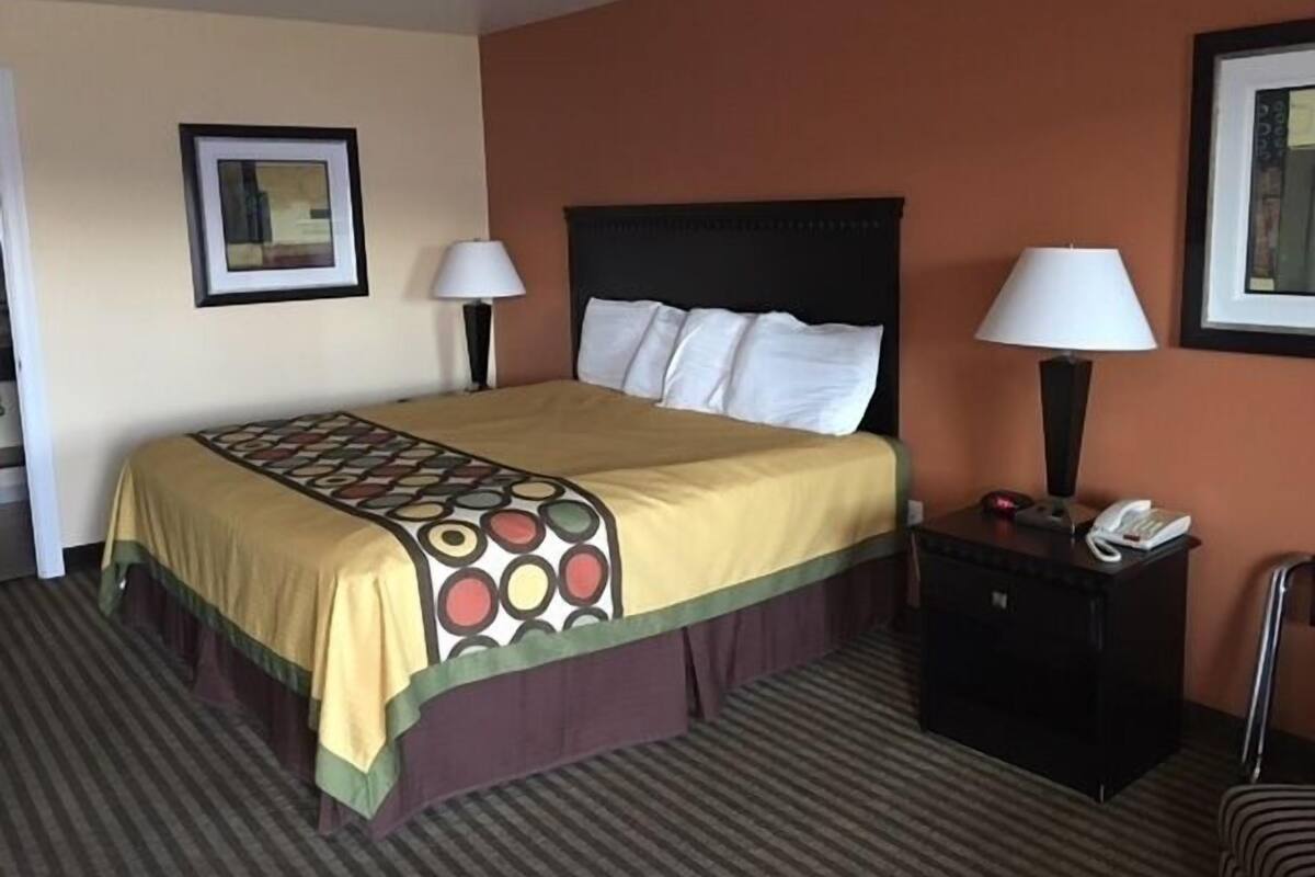 A hotel room with a bed, two bedside lamps, a nightstand with a phone, and a framed picture on the wall.