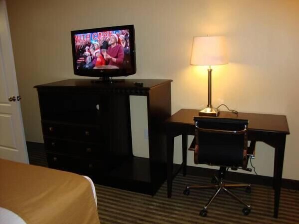 A hotel room with a television on a black stand, a desk with a lamp, and a chair.