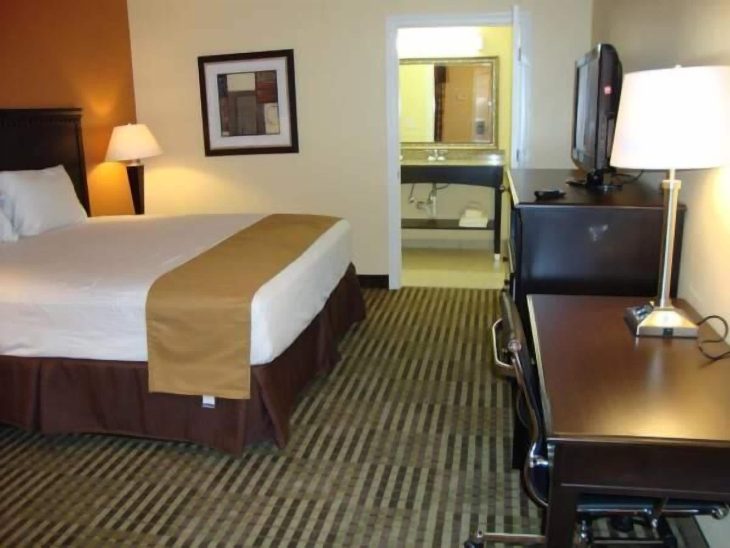 A hotel room with a bed, a desk, a television, and a mirror.