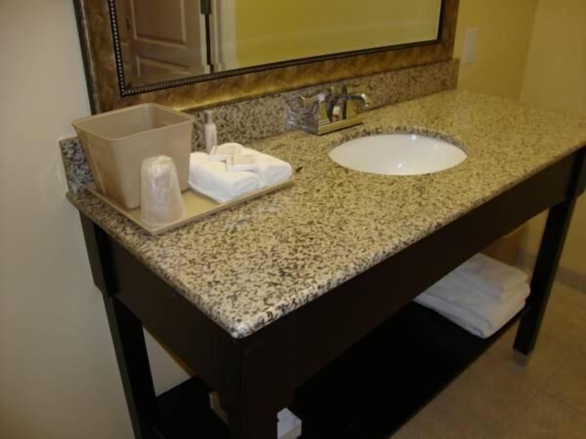 A bathroom with a granite countertop, a white sink, a mirror, and a towel rack.