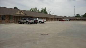A motel with a row of rooms, a parking lot, and a few vehicles parked.