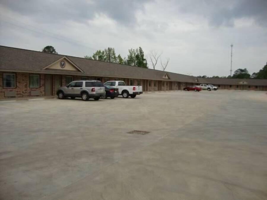 A motel with a row of rooms, a parking lot, and a few vehicles parked.