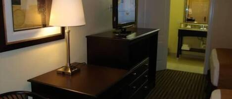 Une chambre d’hôtel équipée d’un bureau, d’une chaise, d’une télévision, d’un lit et d’une salle de bain visible à travers une porte ouverte.