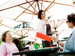 A person handing over a red folder to another individual at an outdoor event with umbrellas. - Mercure Szekesfehervar Magyar Kiraly (Szekesfehervar)