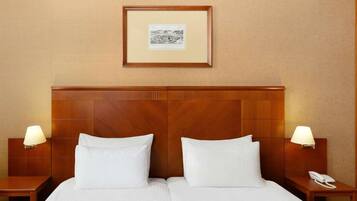 A hotel room with a wooden headboard, two white pillows, a framed picture on the wall, and bedside lamps.