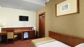 A hotel room with a bed, a desk with a chair, a television, and a small refrigerator.