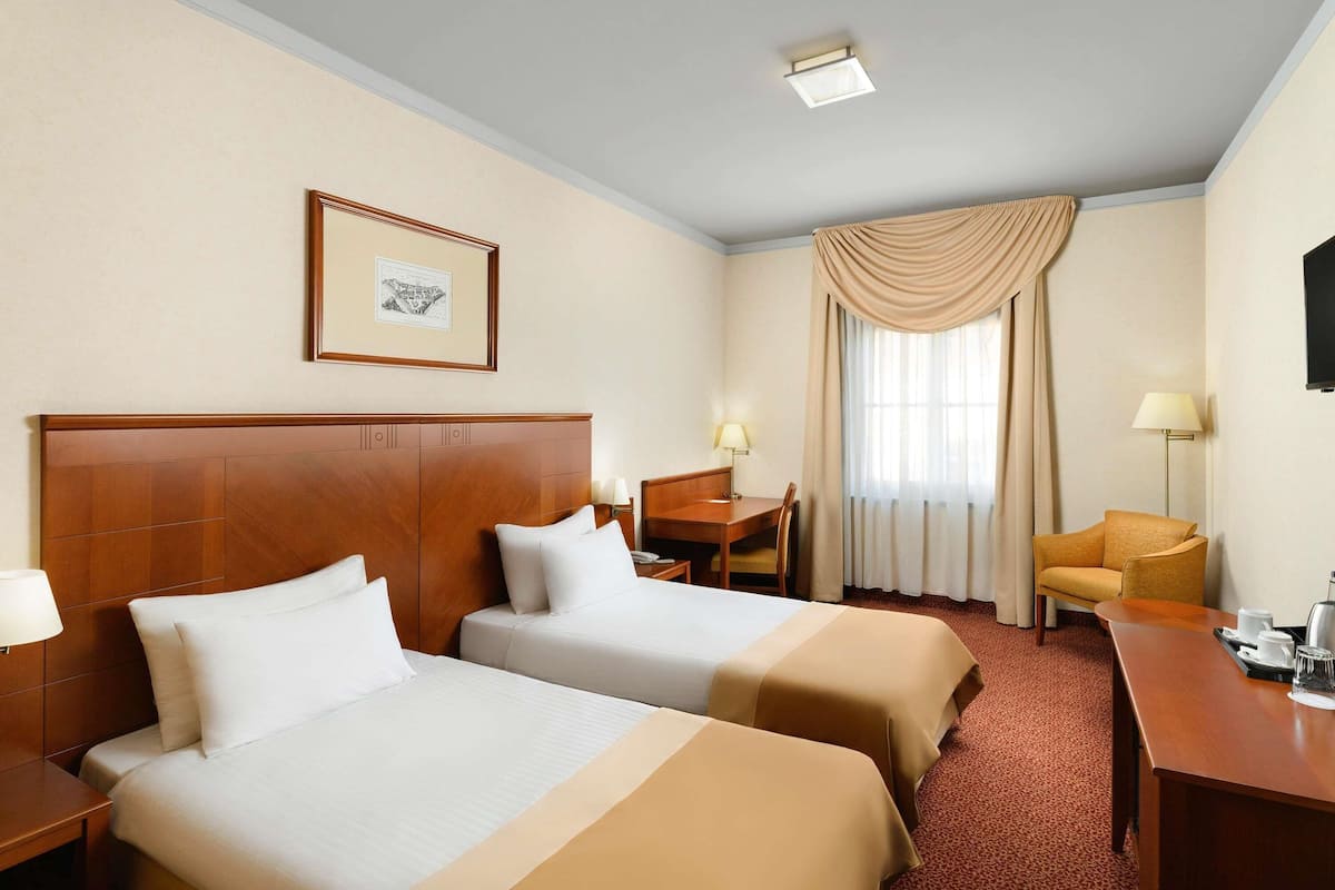 Ein Hotelzimmer mit zwei Betten, einem Schreibtisch, einem Stuhl, einer Lampe und einem fenster mit Vorhängen.