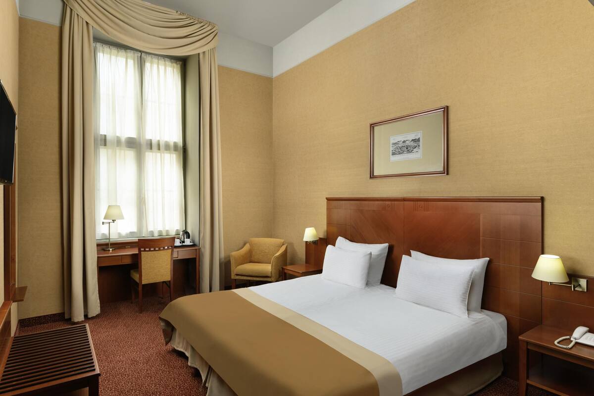 Ein Hotelzimmer mit einem großen Bett, einem Schreibtisch mit Stuhl, einem Telefon und einem Bild an der Wand.