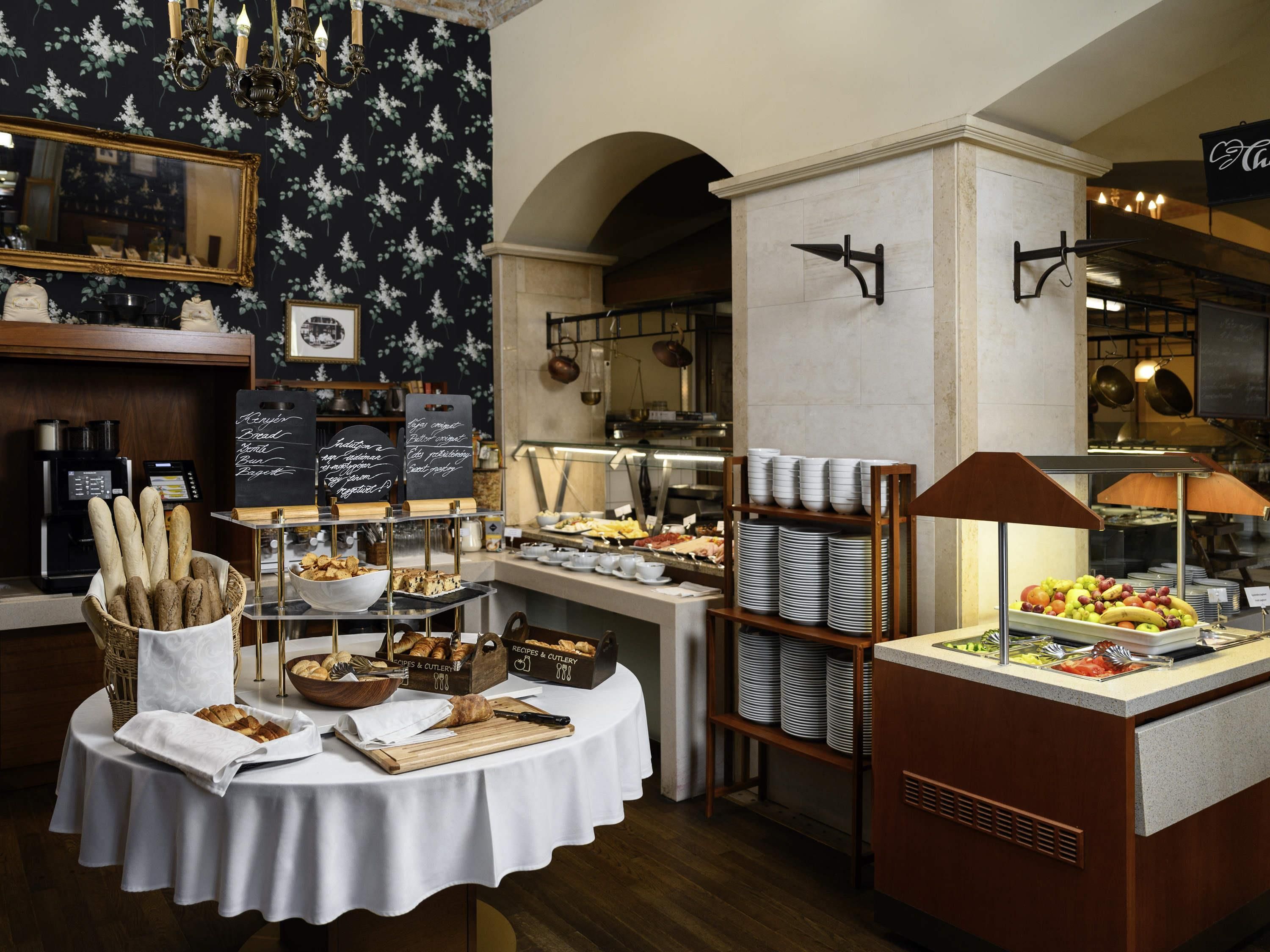 Uma mesa de buffet com diversos alimentos, uma máquina de café e um cardápio em lousa.