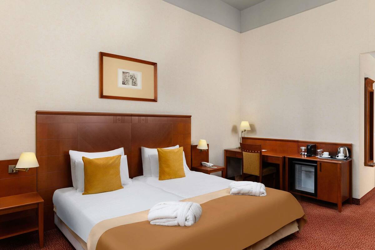 Ein Hotelzimmer mit einem großen Bett, zwei Nachttischen, einem Schreibtisch und einem Spiegel.