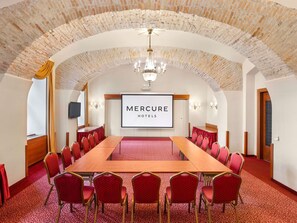 Une salle de conférence avec une longue table, des chaises rouges, un lustre et un écran affichant le logo « Mercure Hotels ».