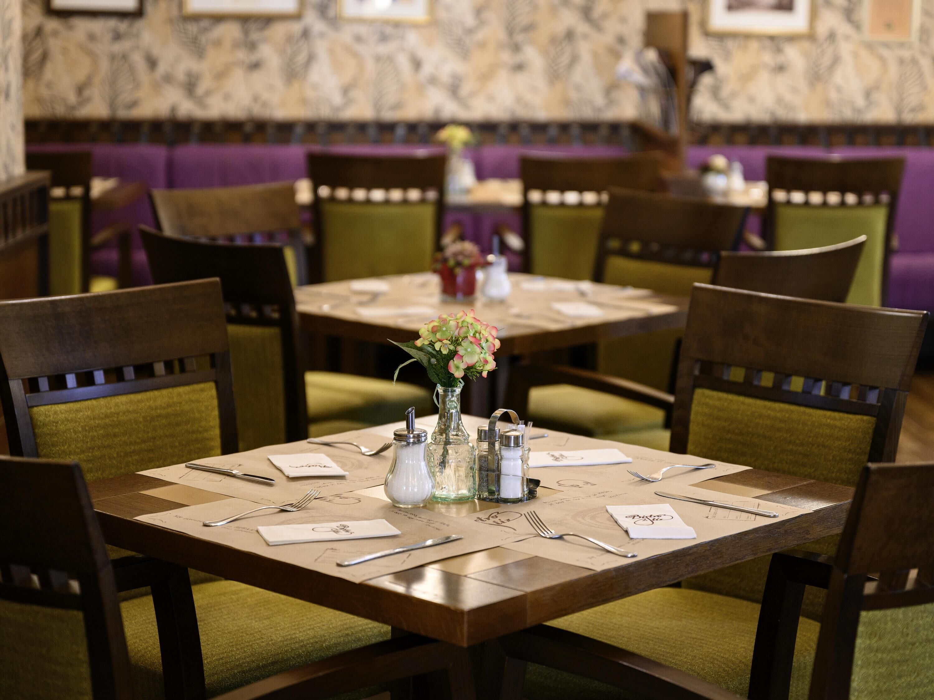 A restaurant with a wooden table set for four, surrounded by green upholstered chairs.