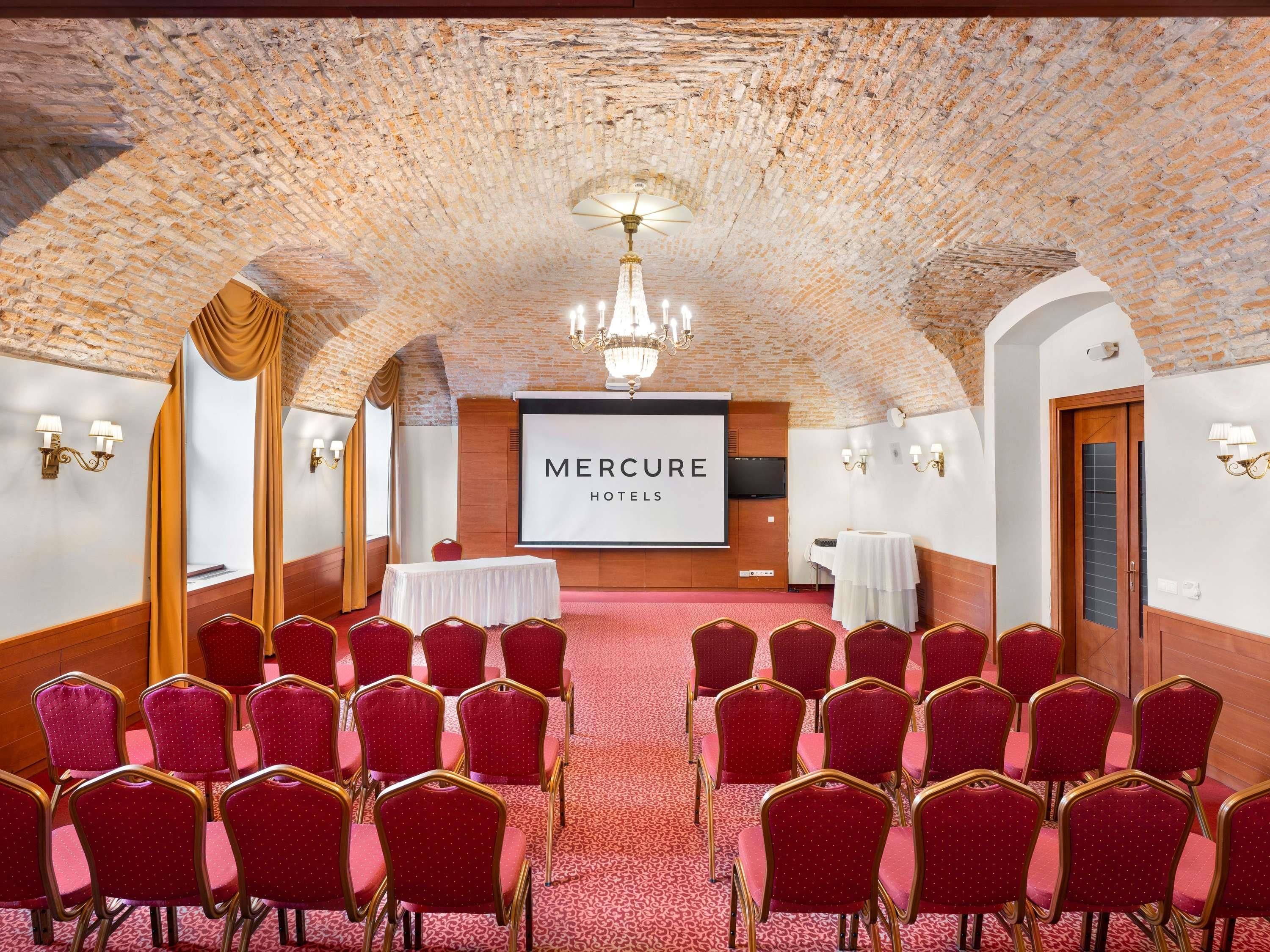 A conference room with a brick ceiling, red chairs, a projector screen, and a chandelier.