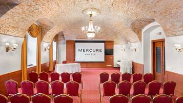A conference room with a brick ceiling, red chairs, a projector screen, and a chandelier.