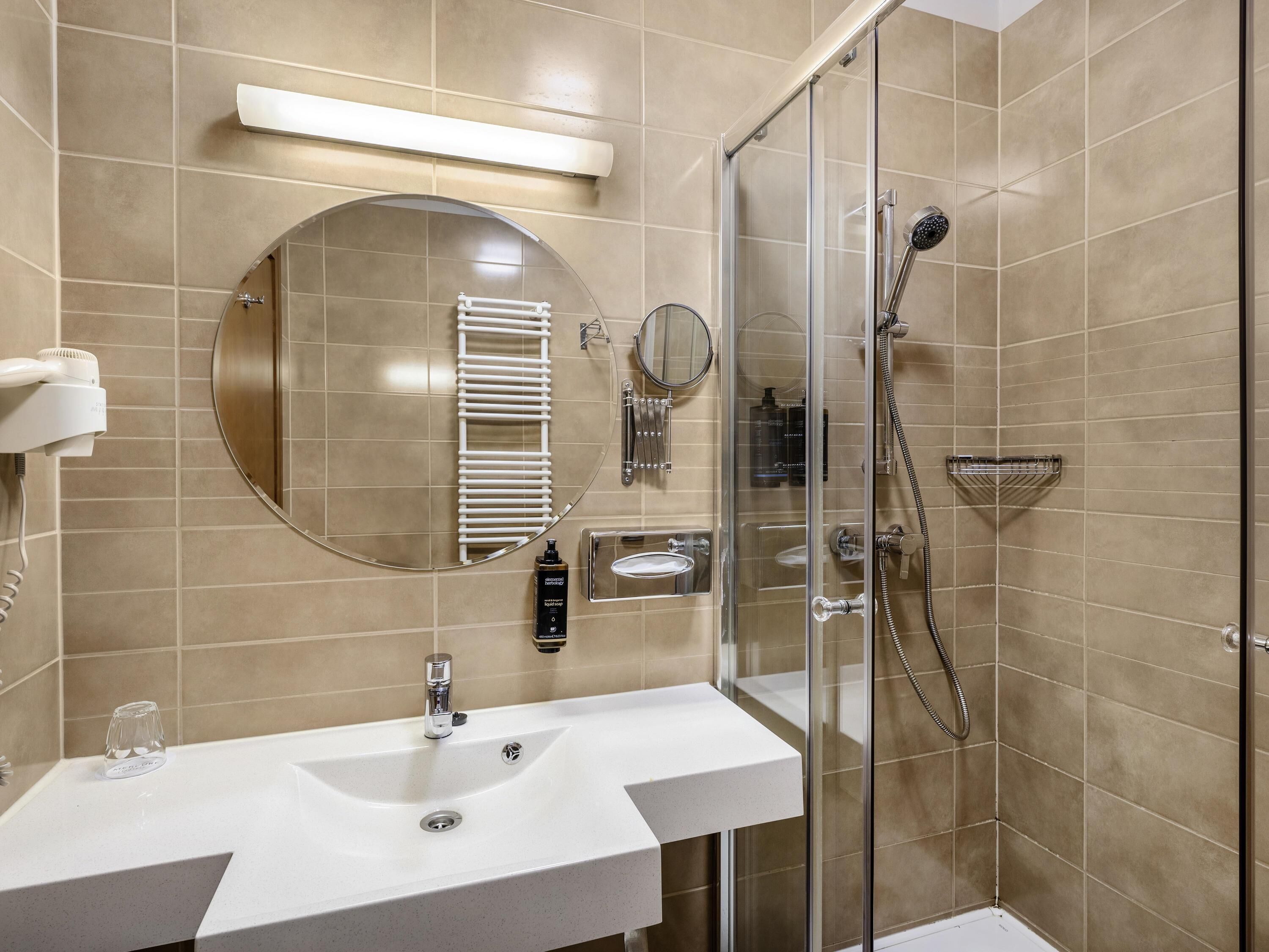 Een badkamer met een wastafel, spiegel, handdoekrek, douche en een douchecabine met glazen wanden.