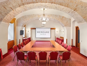 Ein Konferenzraum mit langem Tisch, roten Stühlen, einer Kronleuchter und einem Bildschirm, der 'Mercure Hotels' anzeigt.