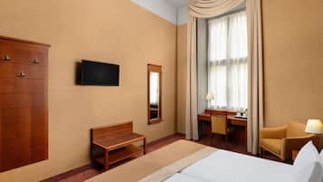 A hotel room with a bed, a desk, a chair, a TV, a wardrobe, and a large window with curtains.