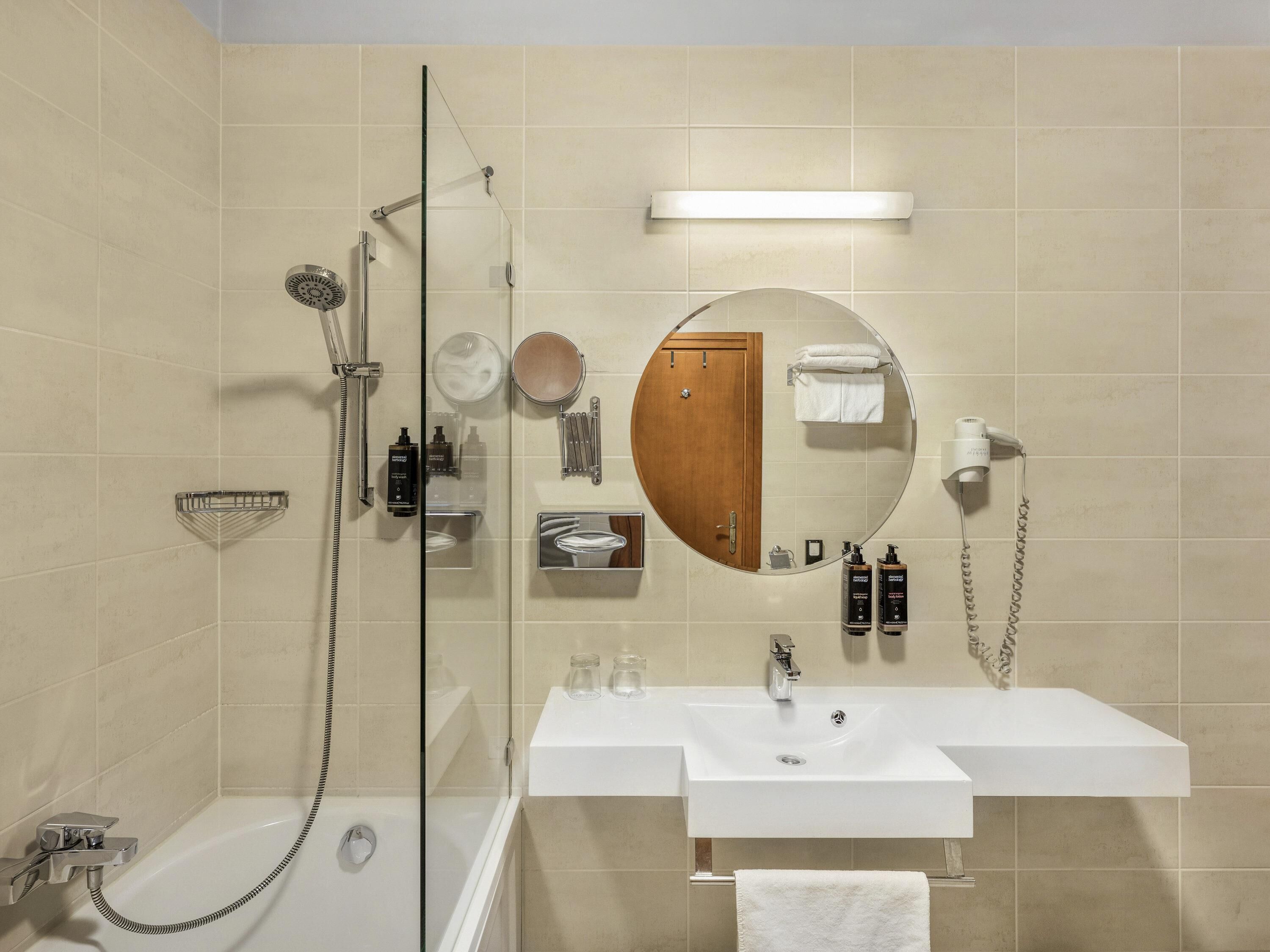 Ein modernes Badezimmer mit einer Duschkabine, einem weißen Waschbecken, einem großen Spiegel und einer Holztür.