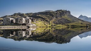 Un complejo moderno de edificios con varias estructuras, incluyendo un edificio central grande y edificios más pequeños adyacentes, ubicado junto a un lago tranquilo con reflejos claros.