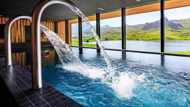 Piscina interior moderna con vistas a un lago y montañas.