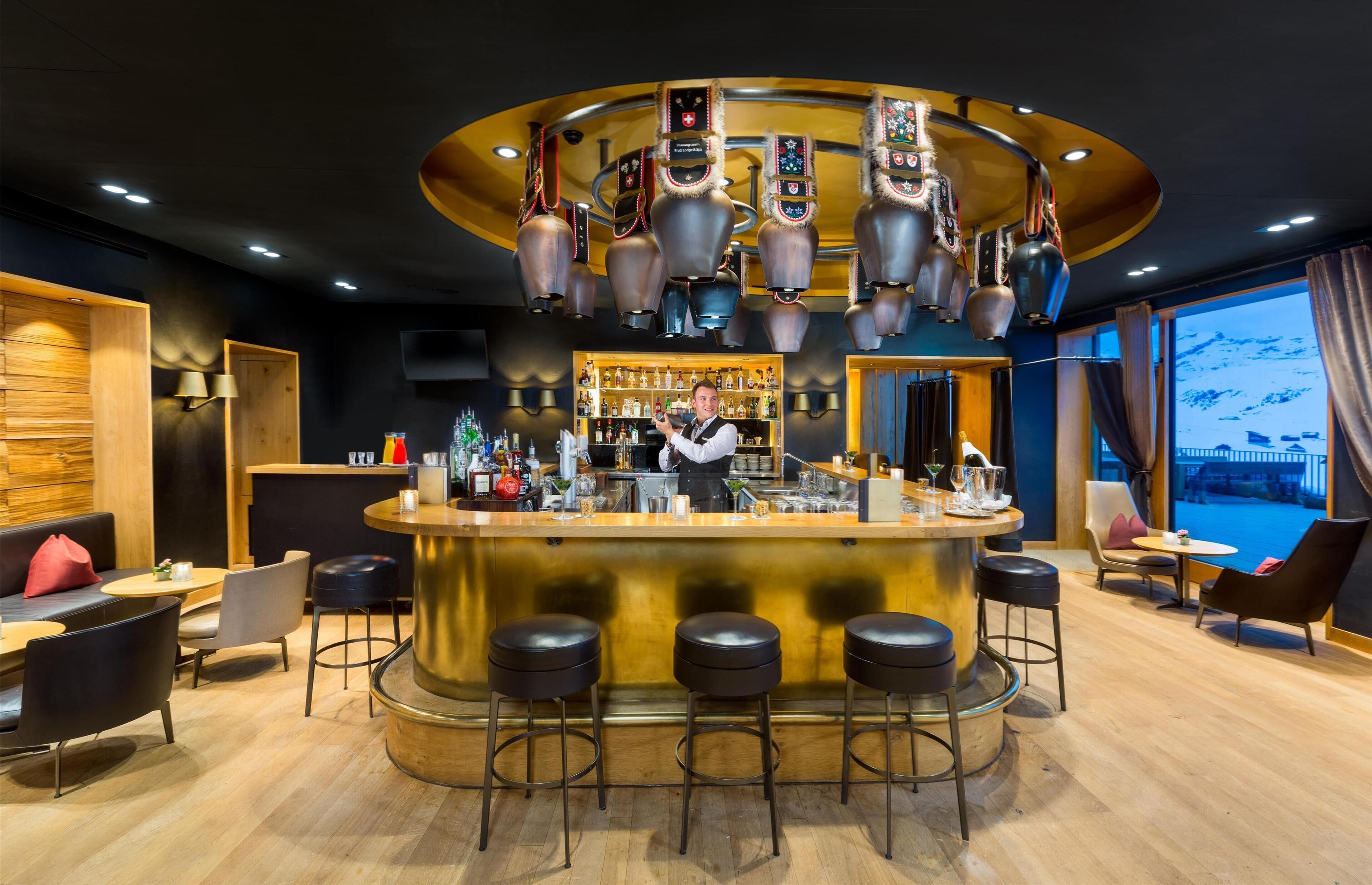 A bar area with a bartender, stools, shelves with bottles, and a view of mountains through large windows.