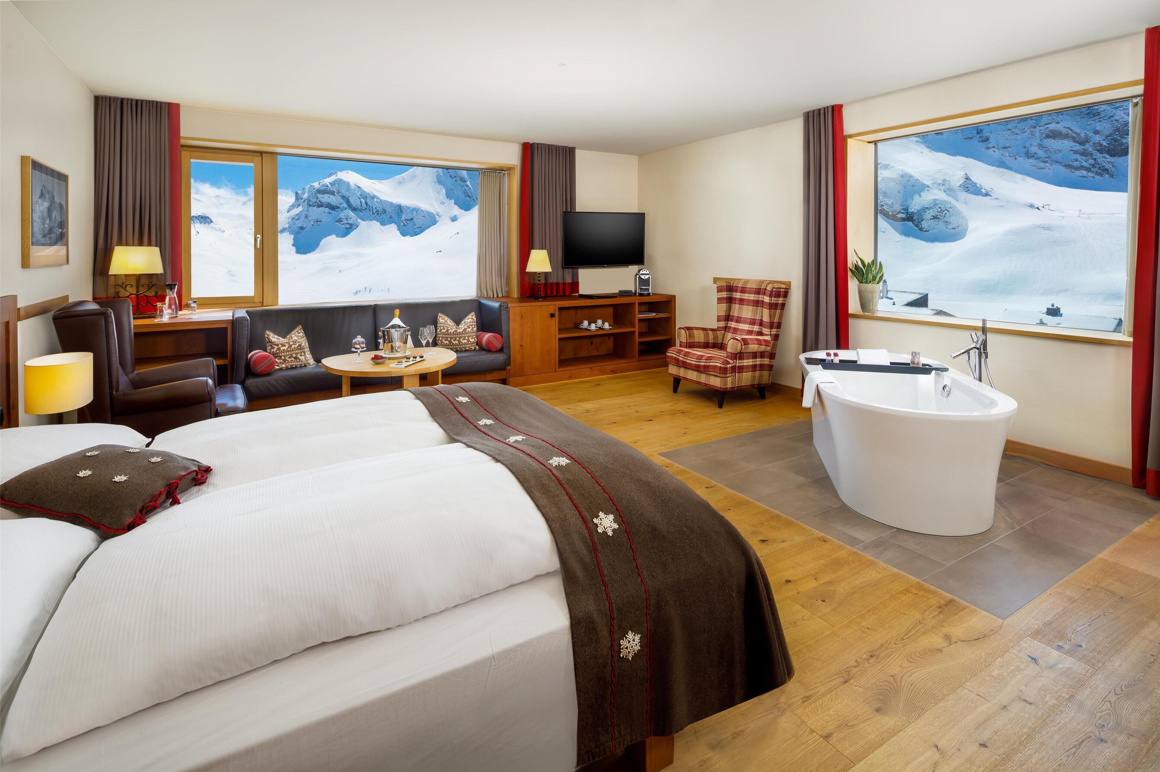 Una habitación de hotel con una cama grande, un sofá, un televisor, una mesita, una silla y una bañera.