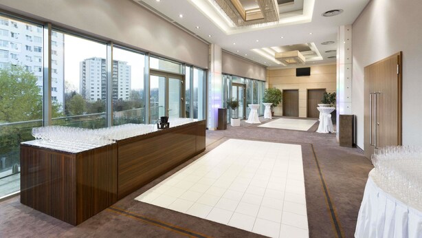 A modern hotel lobby with a reception desk, large windows offering city views, and a spacious layout with tables and chairs. - Ramada by Wyndham Pitesti (Pitesti)