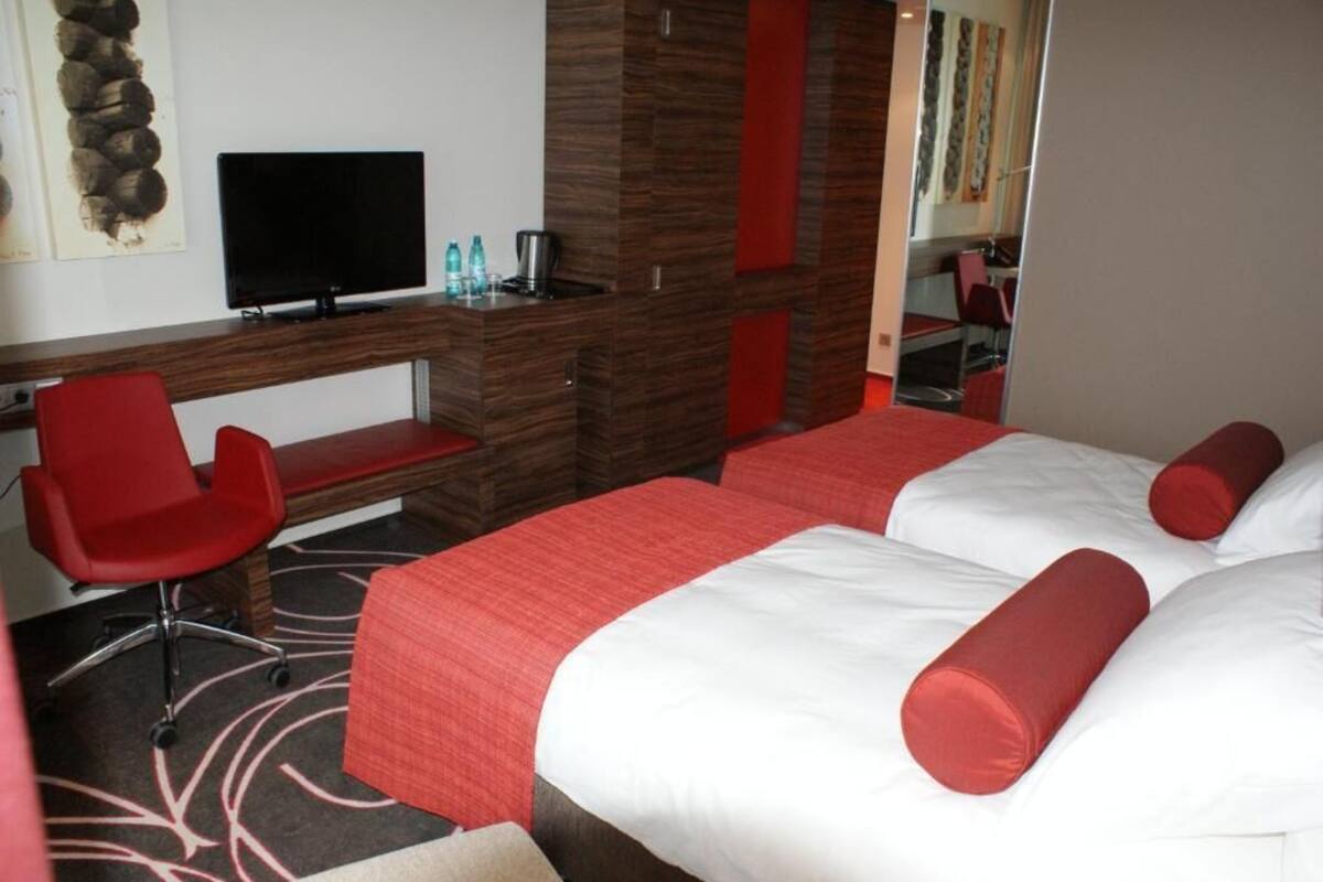 A hotel room with a bed, a desk, a chair, a television, and a mirror.