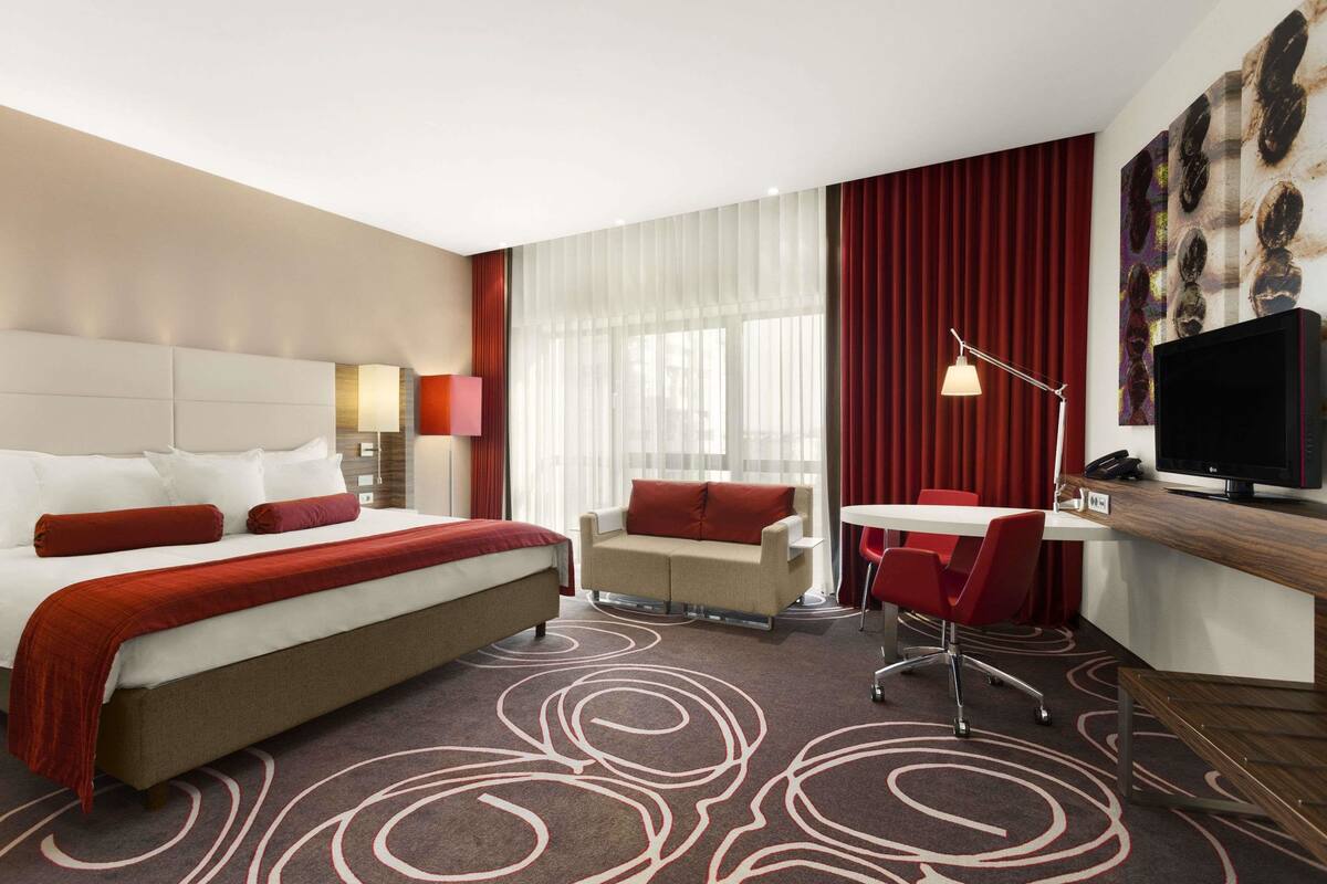 A hotel room with a large bed, a desk with a chair, a small table, and a television.