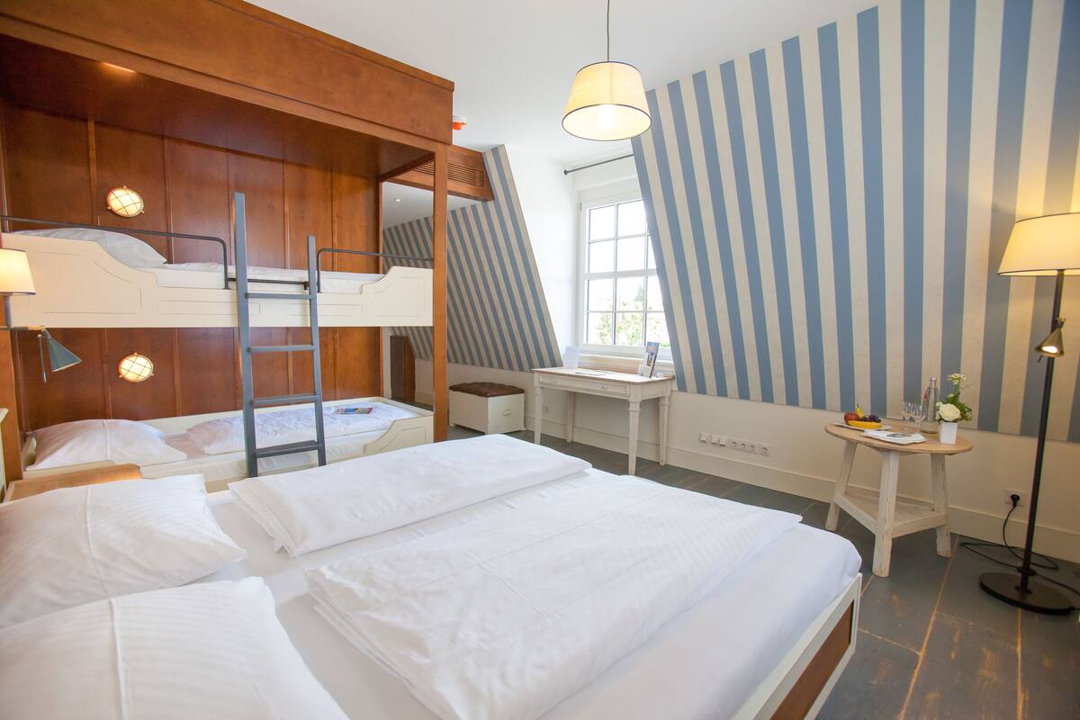 Ein Hotelzimmer mit Etagenbetten, einem Schreibtisch, einem Stuhl, einer Lampe und einem Fenster.