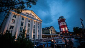 Ein Hotel mit einem markanten Leuchtturm im Hintergrund, einer Uferpromenade und einer gut beleuchteten Fassade.